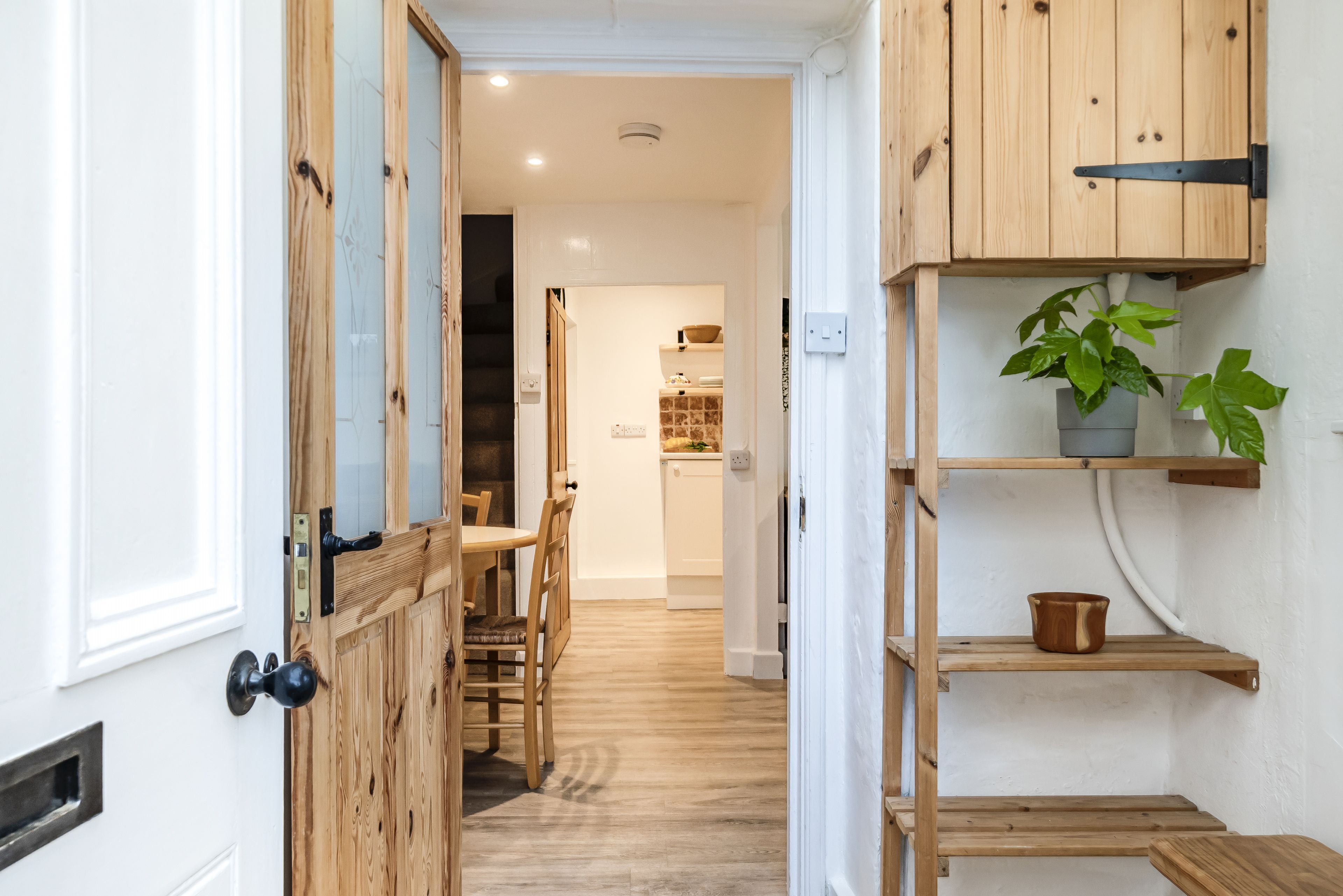A hallway with wooden doors and shelves, leading to a dining area with a table and chairs.