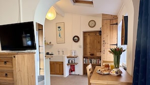 A cozy kitchen with wooden cabinets, a dining table with breakfast, and a TV on a stand. - Meads Cabin - Charmouth, Lyme Regis (Charmouth)