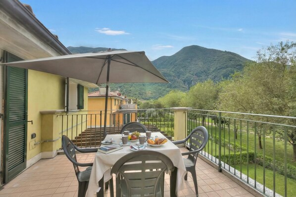 A balcony with a table set for breakfast, a chair, and a large umbrella. - Porto Letizia Orchidea 5, Porlezza, Italy (Porlezza)