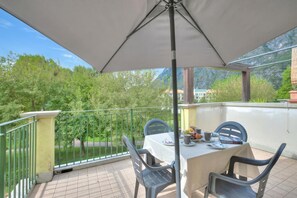 A balcony with a table, chairs, and an umbrella. - Porto Letizia Orchidea 5, Porlezza, Italy (Porlezza)