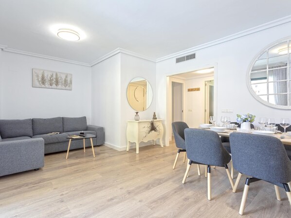 Una sala de estar moderna con un sofá gris, una mesita redonda y un comedor con una mesa y sillas redondas.