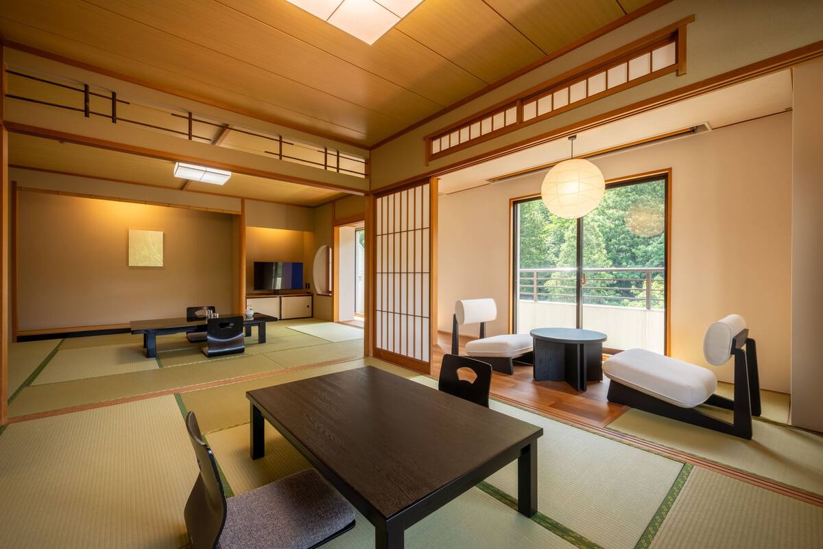 Um quarto japonês tradicional com tatames, uma mesa baixa e uma porta deslizante que dá para uma varanda.