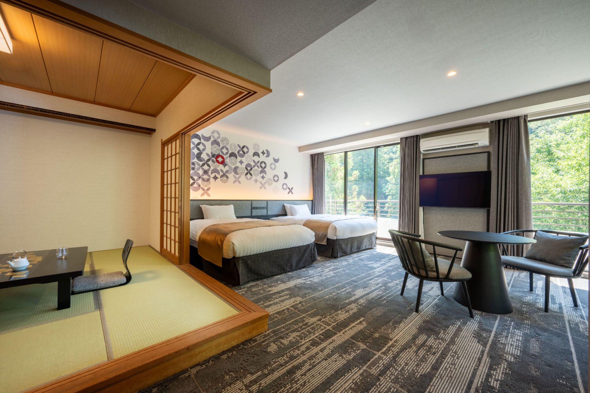 Habitación de hotel con zona de estar con esterilla de tatami tradicional, cama con dos almohadas, televisor y mesa de comedor con sillas.