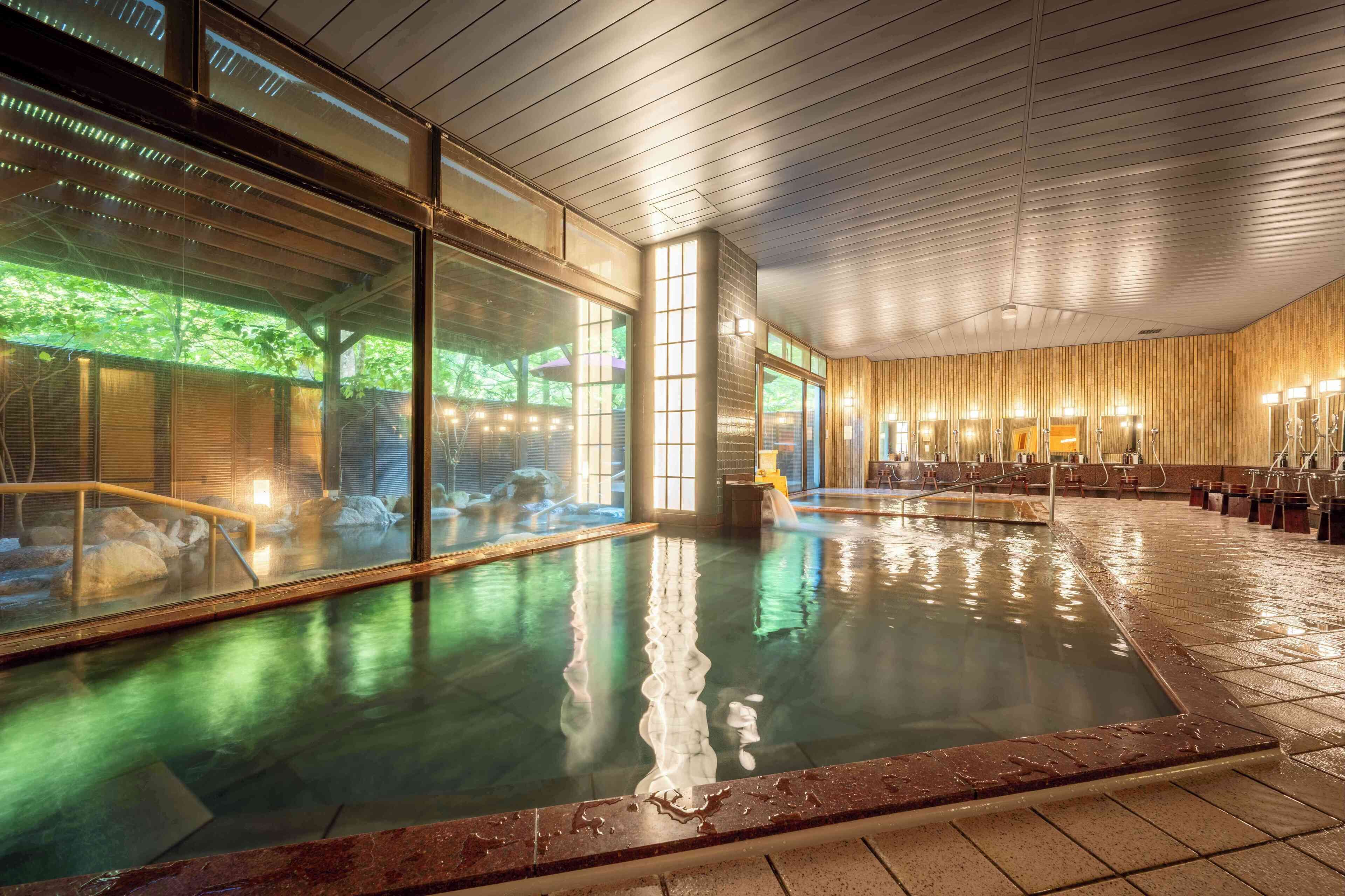 A spacious indoor pool with clear glass walls, wooden paneling on the walls, and a tiled floor.