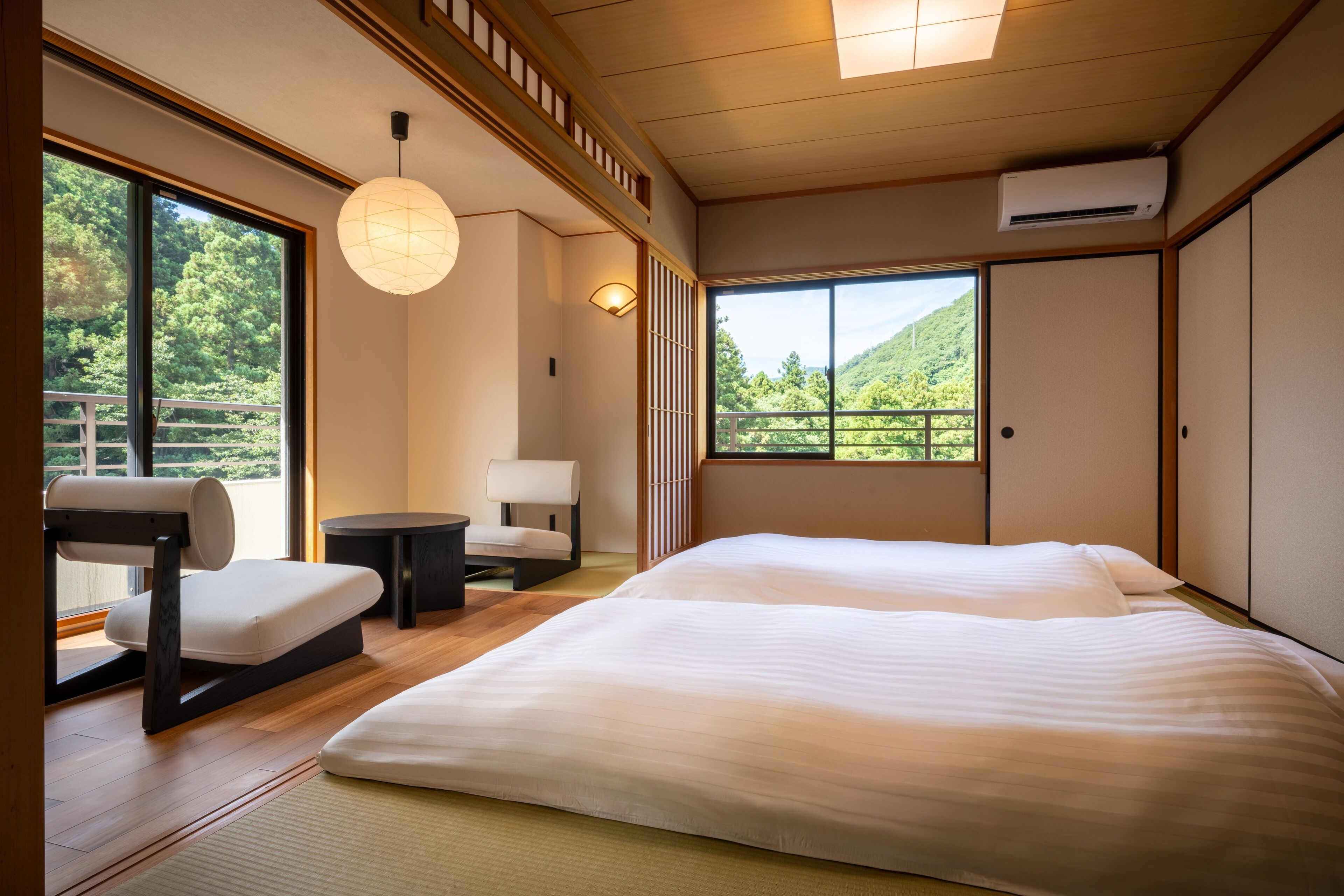 A modern hotel room with a large bed, a seating area, and a view of a forested area.