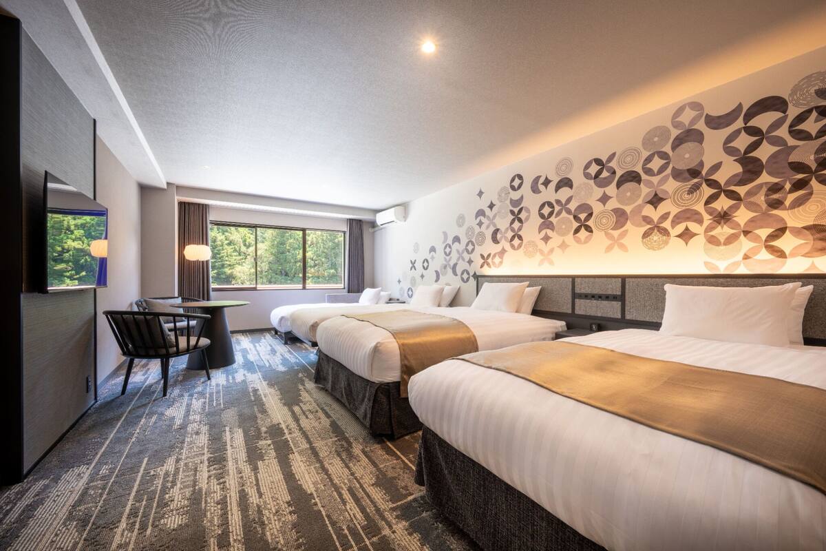Quarto de hotel com duas camas, uma escrivaninha e uma janela grande.