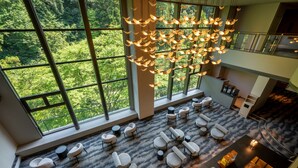 A spacious lounge area with multiple seating options, large windows offering a view of a forest, and a unique hanging light fixture. - Yamanaka Onsen KAJIKASO (Kaga)
