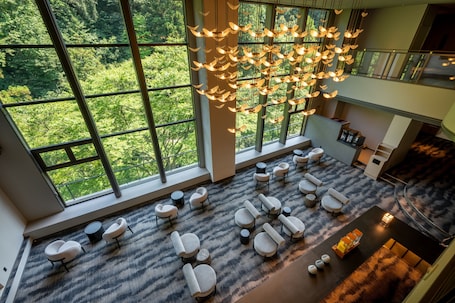 A spacious lounge area with multiple seating options, large windows offering a view of a forest, and a unique hanging light fixture.