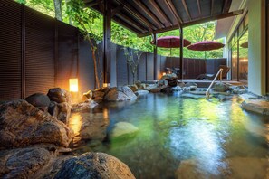 A serene indoor hot spring area with a wooden deck, large rocks, and a small waterfall. - Yamanaka Onsen KAJIKASO (Kaga)