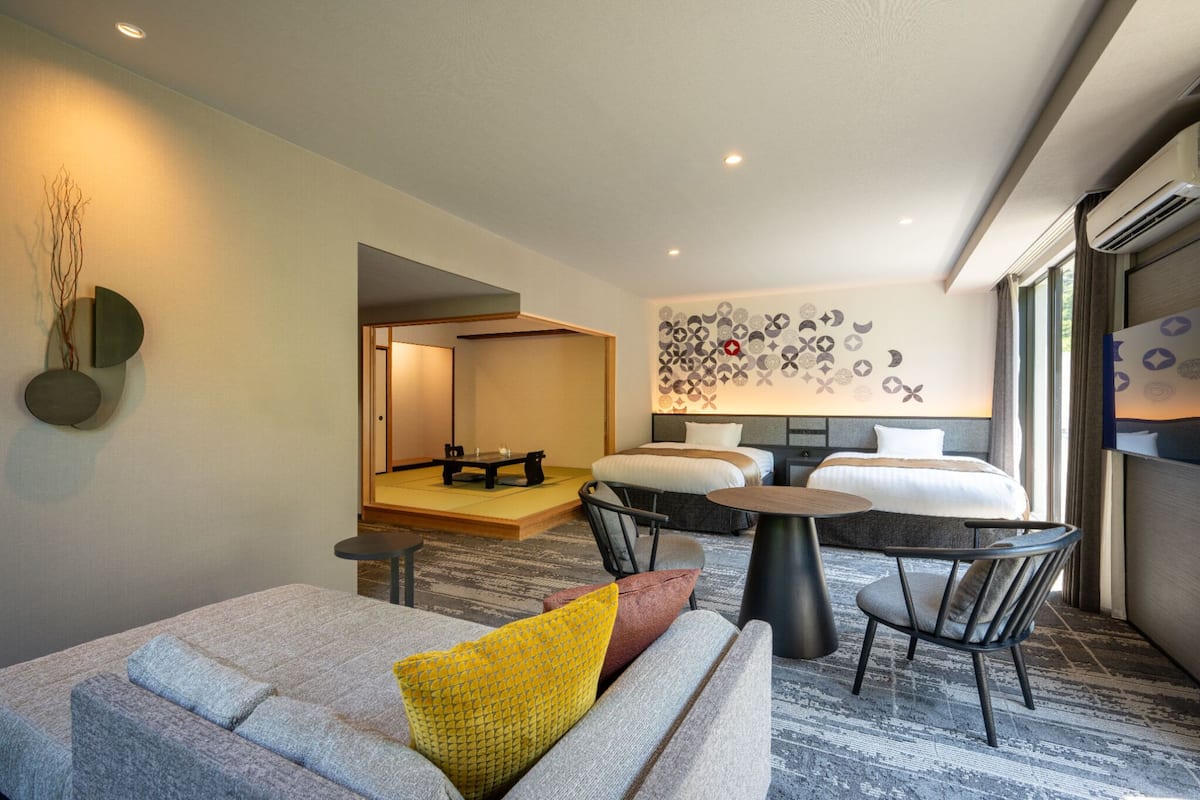 Quarto de hotel moderno com sofá, duas camas, uma mesa de jantar e uma decoração de parede.