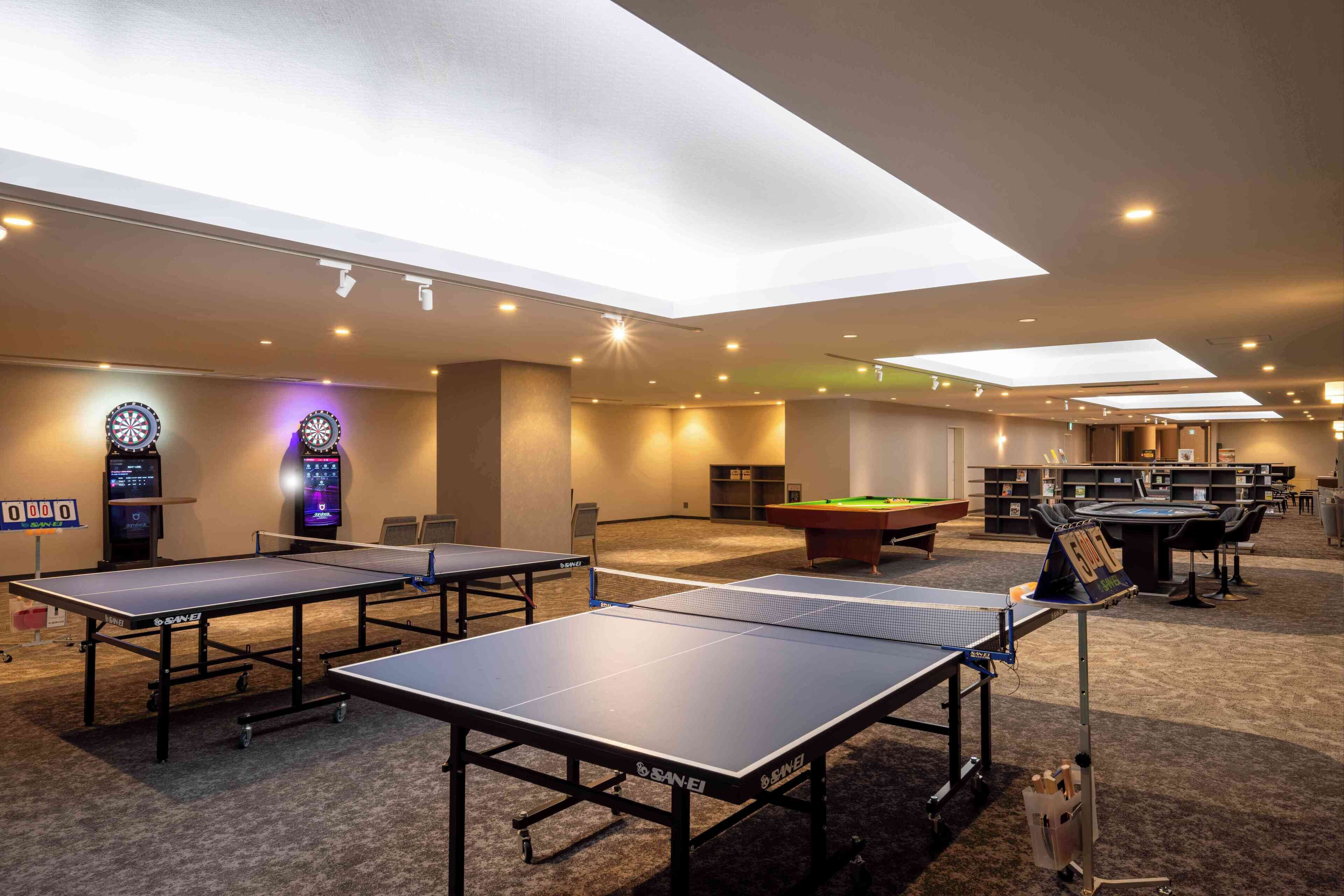 A room with ping pong tables, a pool table, and dartboards.