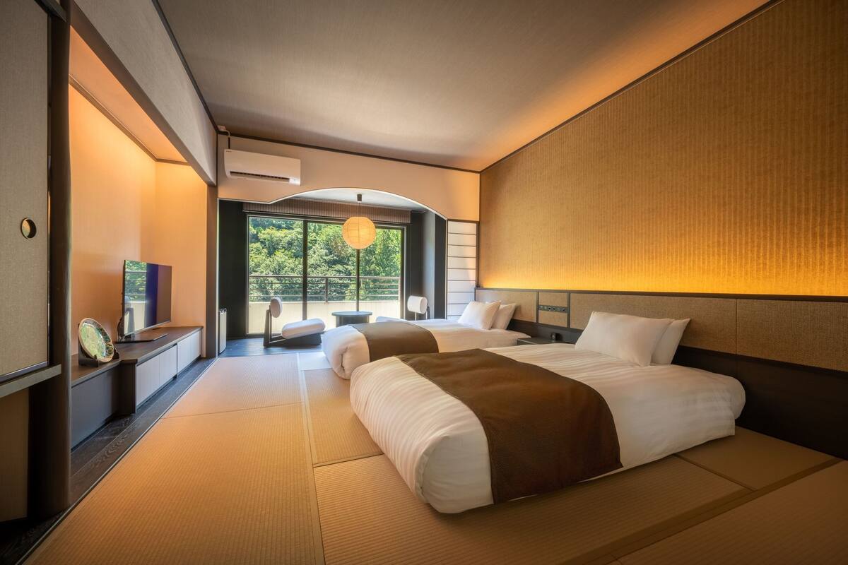 Quarto de hotel com uma cama grande, televisão, escrivaninha e vista para o exterior.