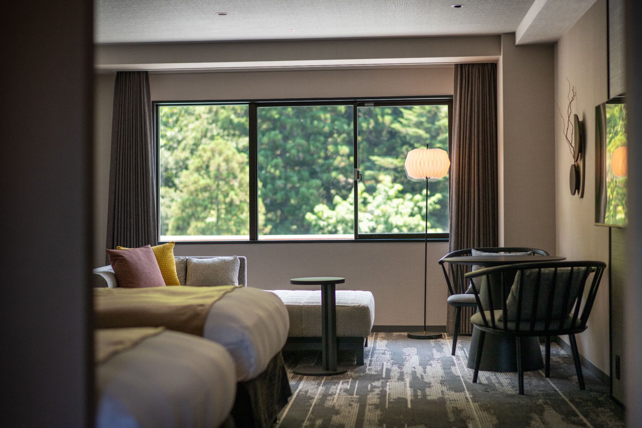 Una habitación de hotel con un ventanal grande, una cama, una mesita y una silla.