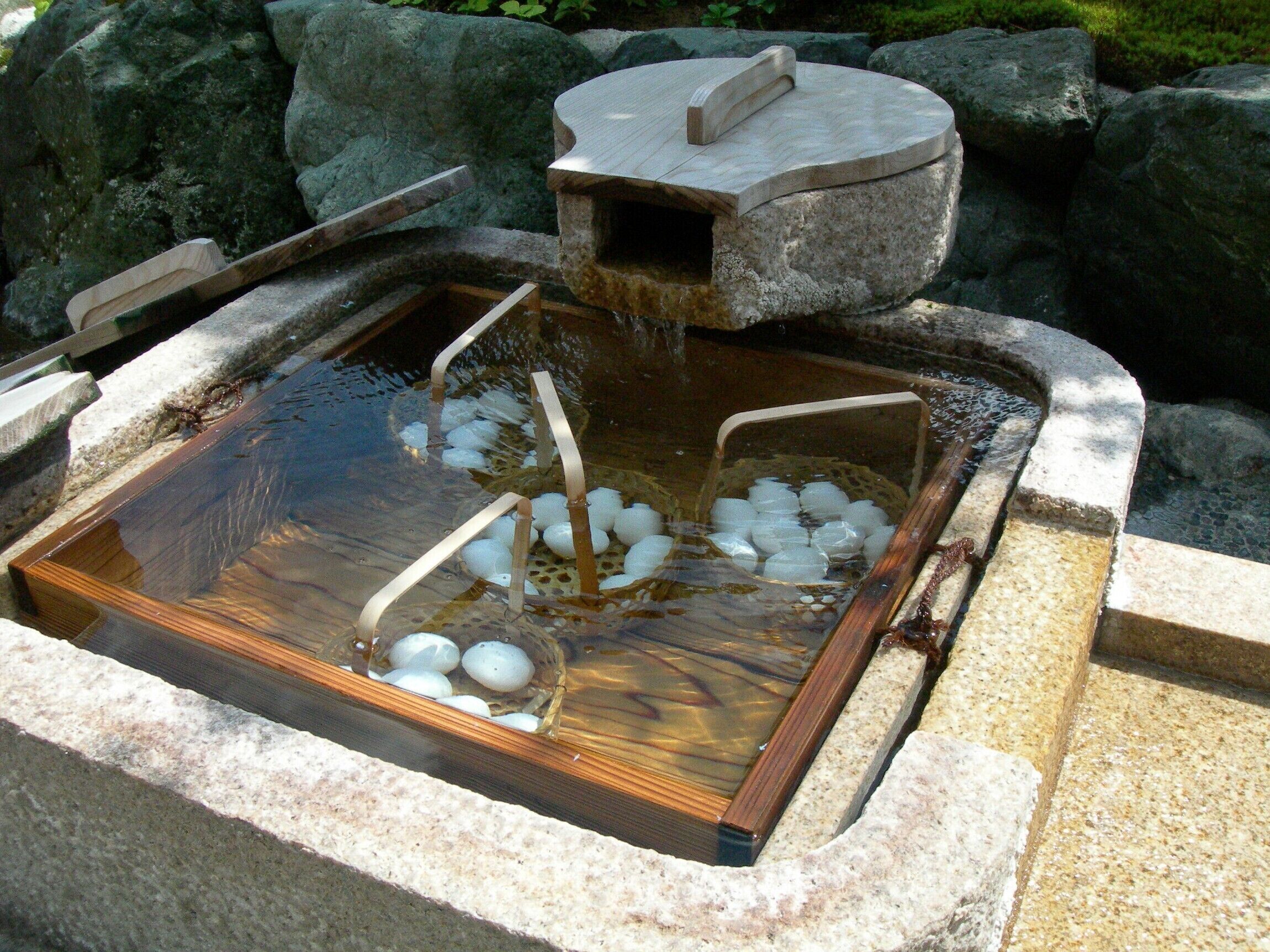 A stone hot spring with a wooden bench and a stone basin filled with ice.