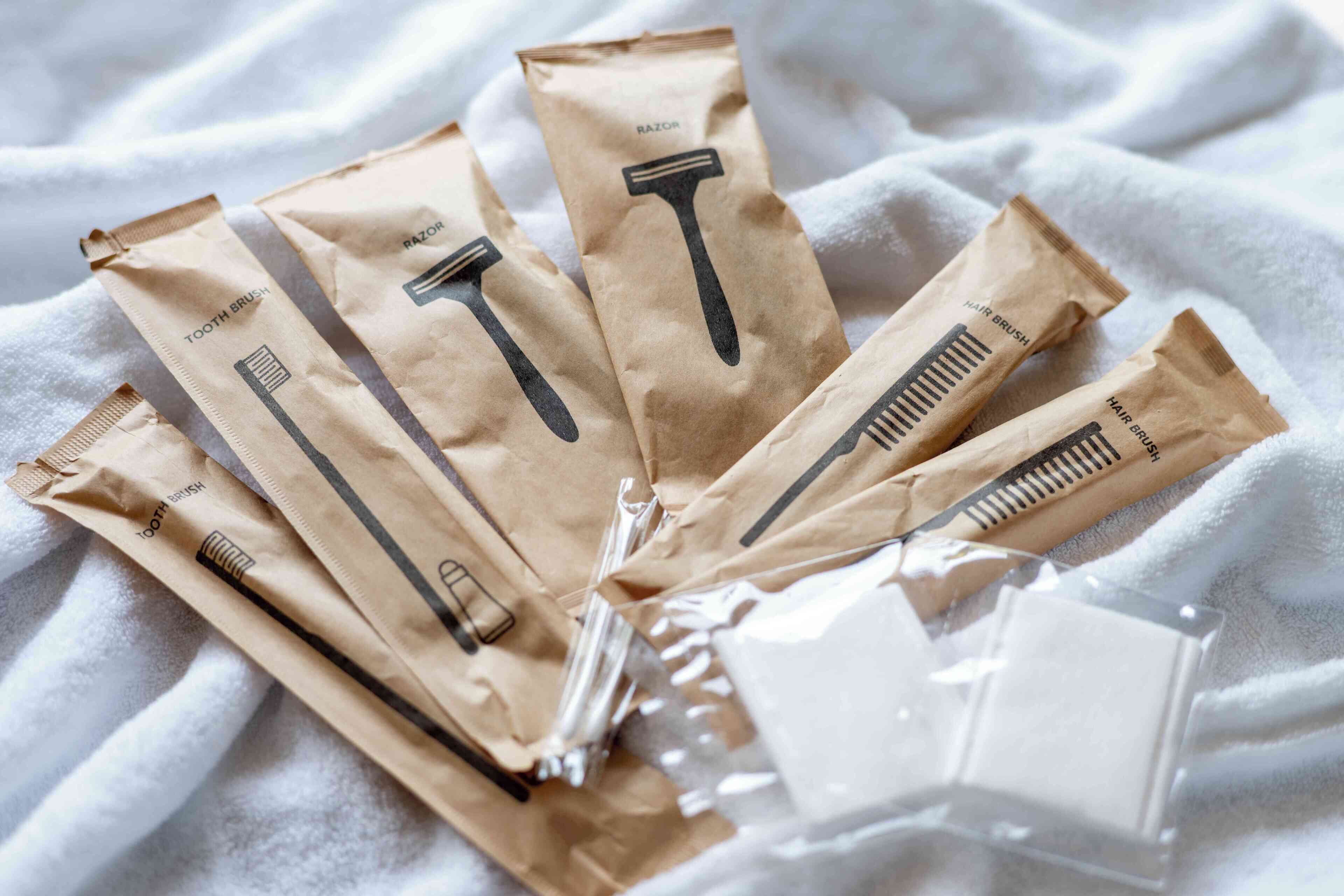 Five brown paper bags with shaving tools labeled "RAZOR" and "TOOTH BRUSH" on a white towel.