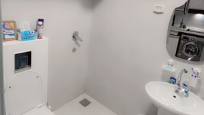 Une petite salle de bain blanche, équipée de toilettes, d’un lavabo et d’un espace douche.