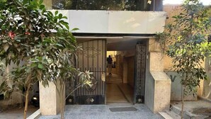 Une entrée fermée par un portail, avec un chemin en béton menant à un bâtiment. De part et d’autre de l’entrée, on trouve des plantes en pot.