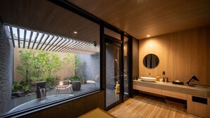Een moderne badkamer met een groot raam, een ronde spiegel en een houten wastafelmeubel.