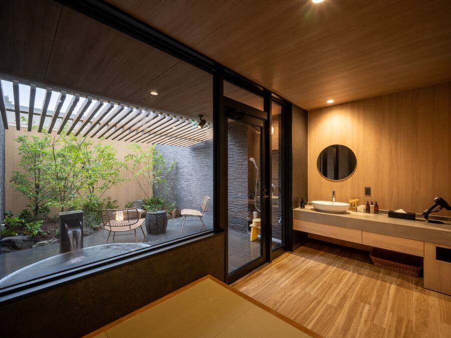 Un baño moderno con un ventanal grande, un espejo redondo y un tocador de madera.