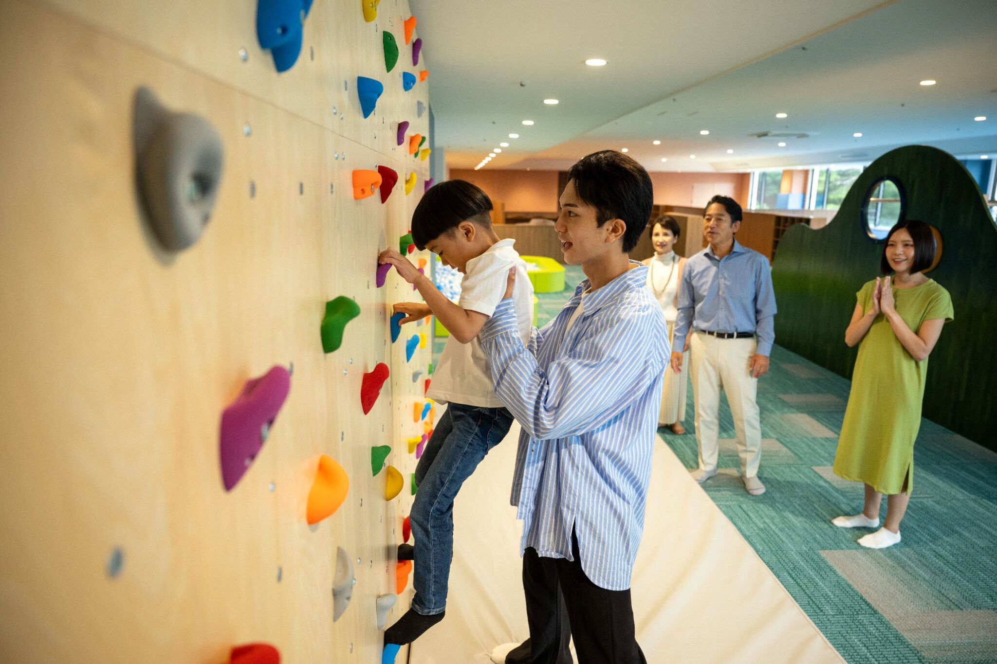 A climbing wall with colorful holds, a group of people, and a green wall feature.