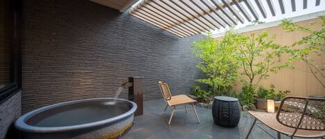 A modern outdoor relaxation area with a hot tub, seating, and a pergola providing shade.