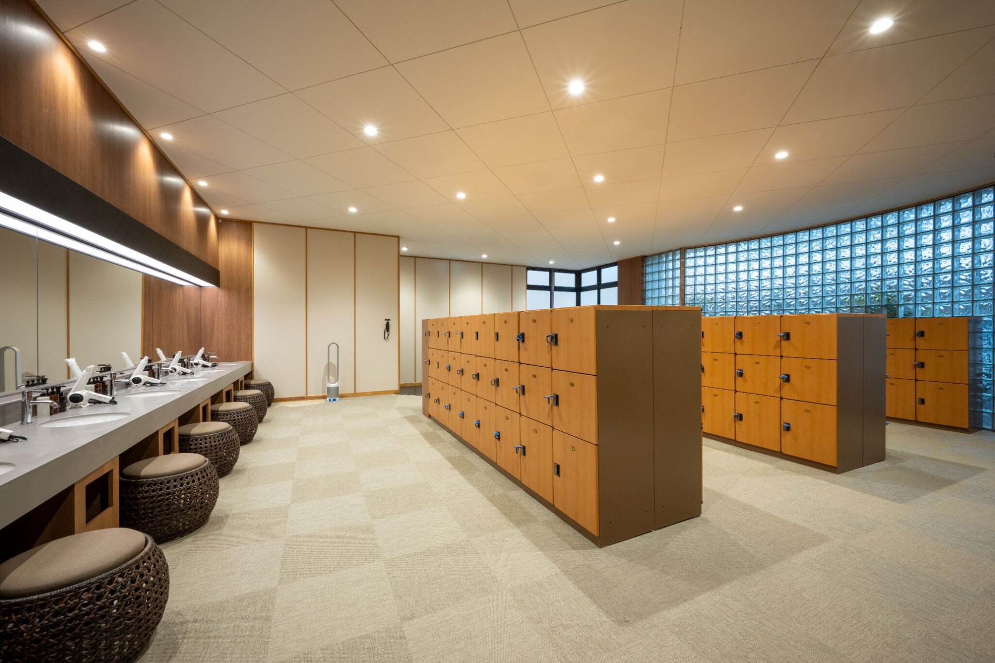 A modern bathroom with multiple sinks, wooden lockers, and a checkered floor.