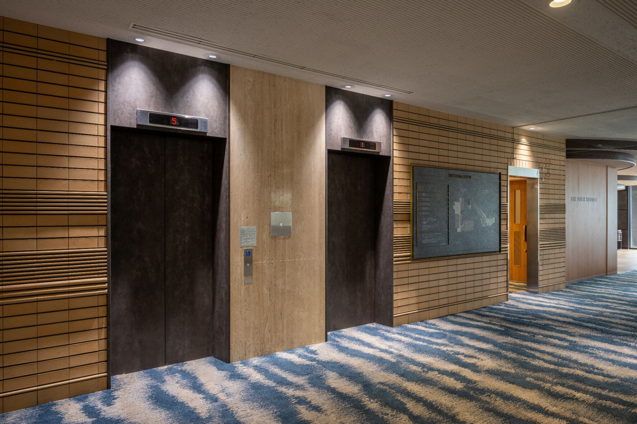 A hotel lobby with two elevators, a digital display, and a framed map on the wall.