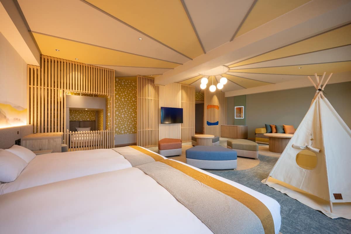A modern hotel room with a large bed, a sofa, a small table, and a teepee.