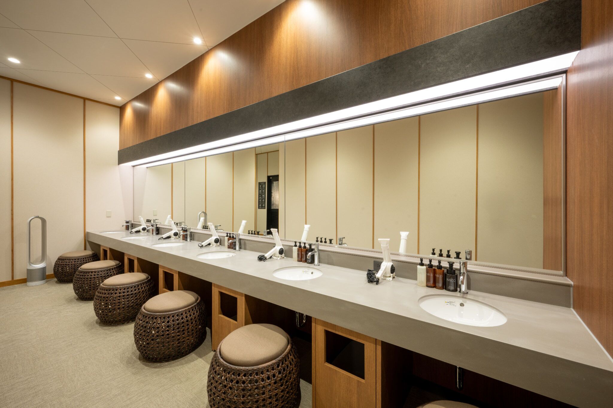 A modern bathroom with three sinks, a large mirror, and wooden accents.