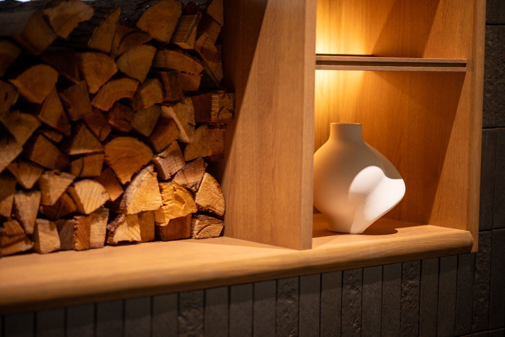 A wooden shelf with a white vase and a stack of firewood.