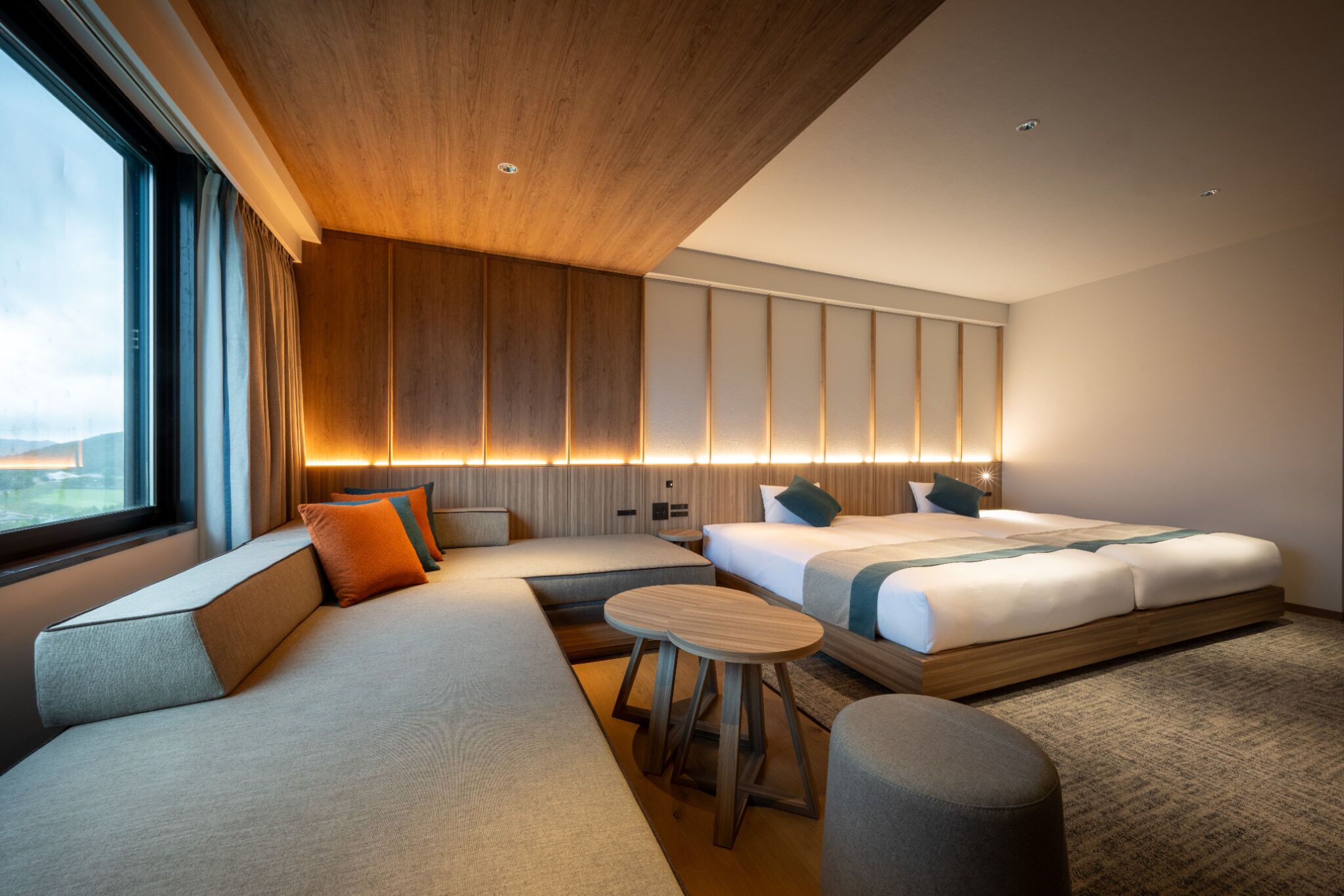 A modern hotel room with a large bed, a sofa, a small table, and a view of the outdoors.