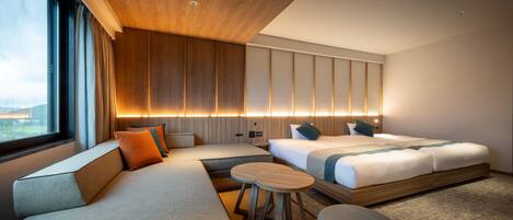 A modern hotel room with a large bed, a sofa, a small table, and a view of the outdoors.