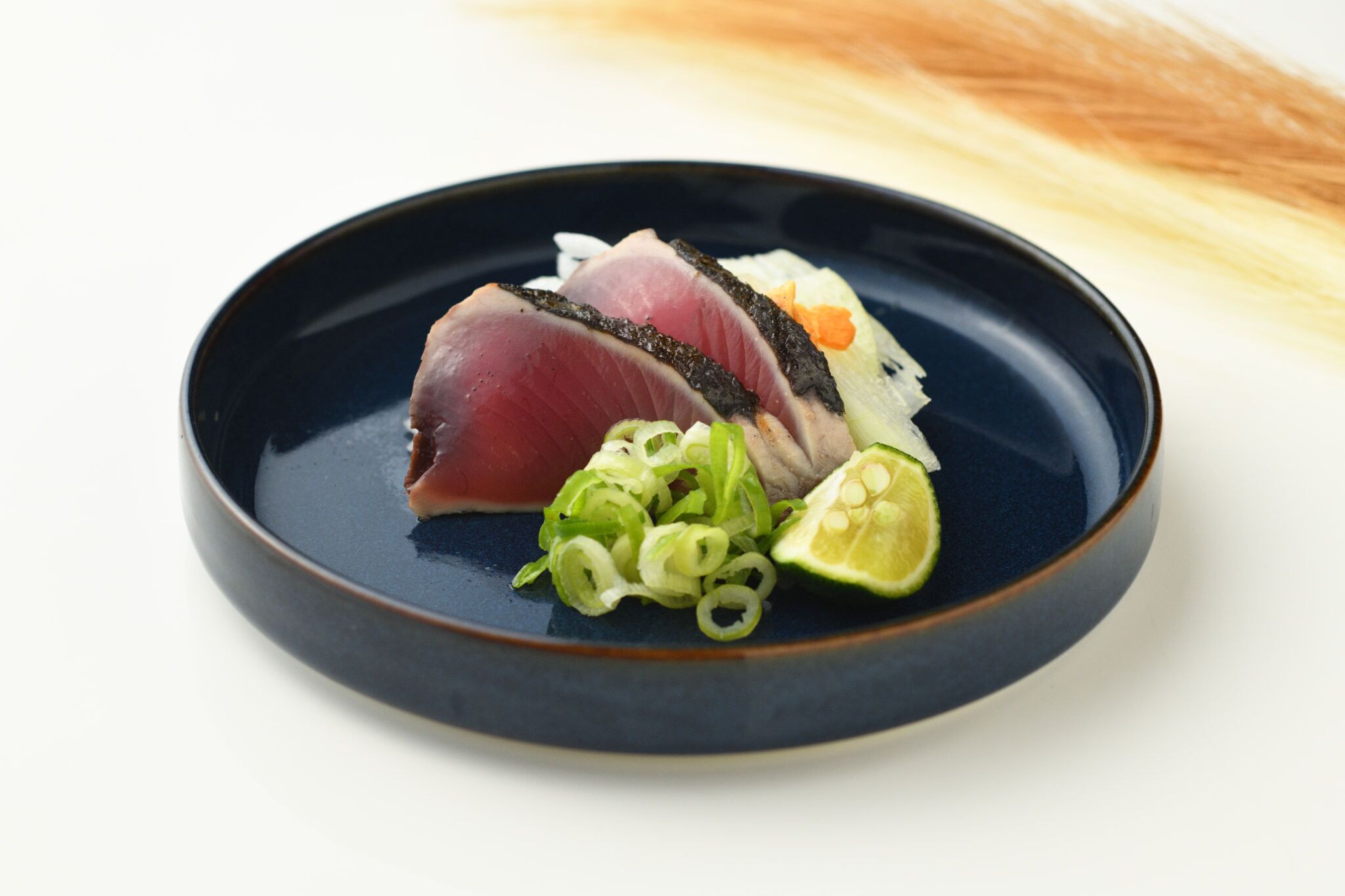 A plate with sliced fish, green onions, and a lime wedge.