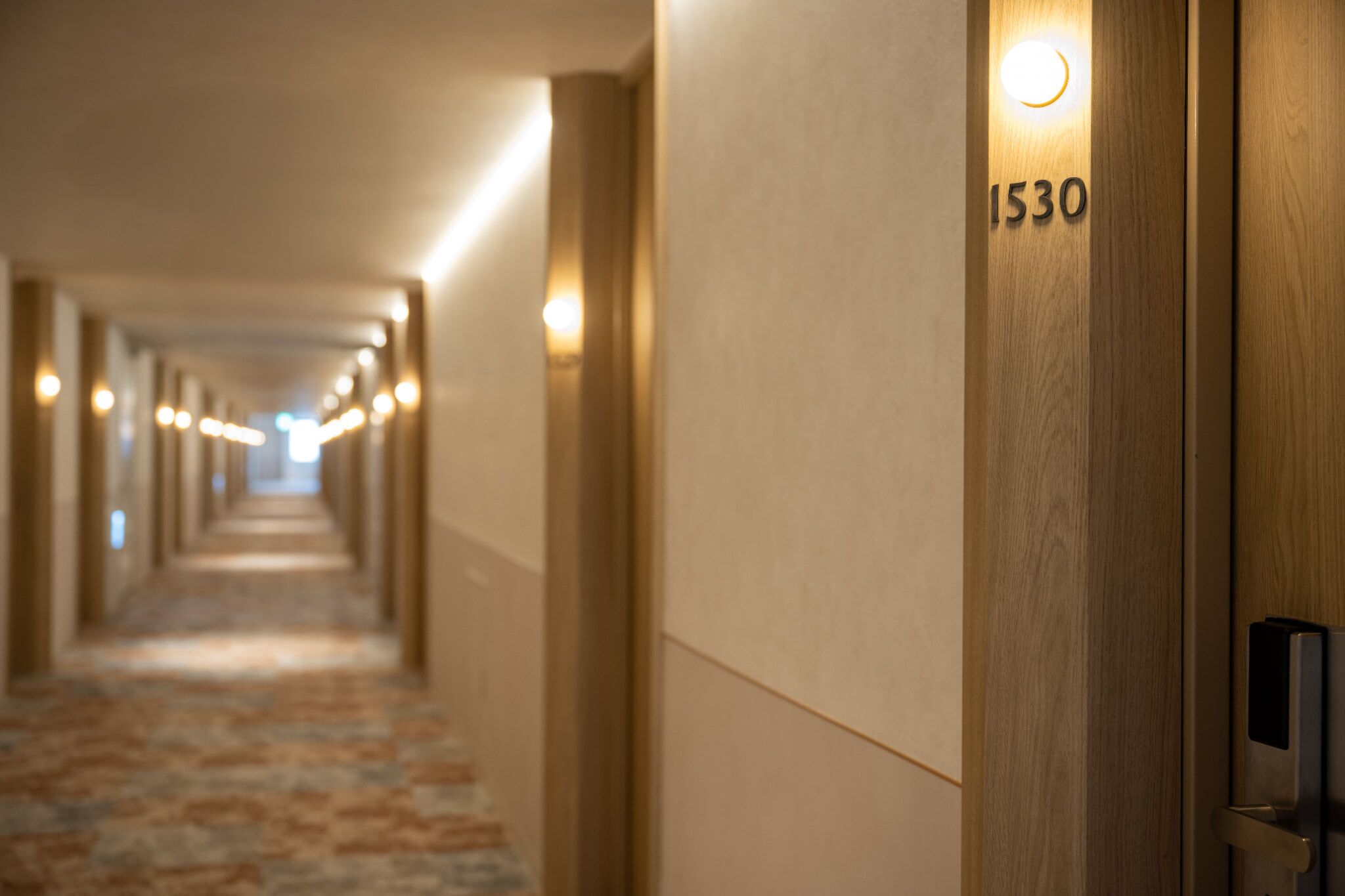 A hotel hallway with a carpeted floor, wooden walls, and illuminated wall sconces.
