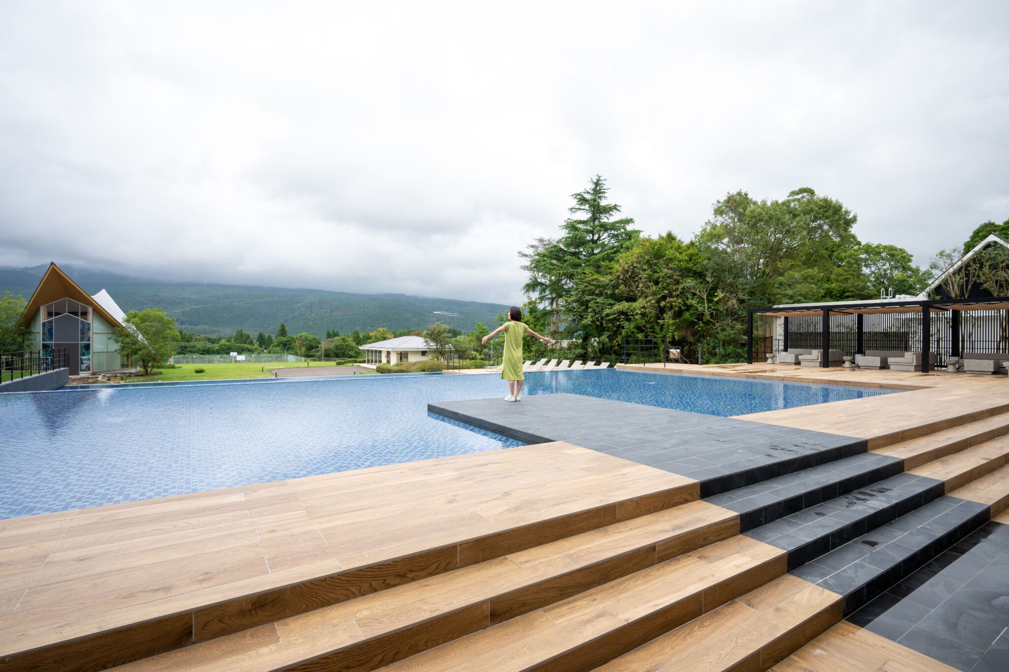 Une piscine avec des marches menant à l’eau, entourée de verdure et bordée d’un paysage montagneux.