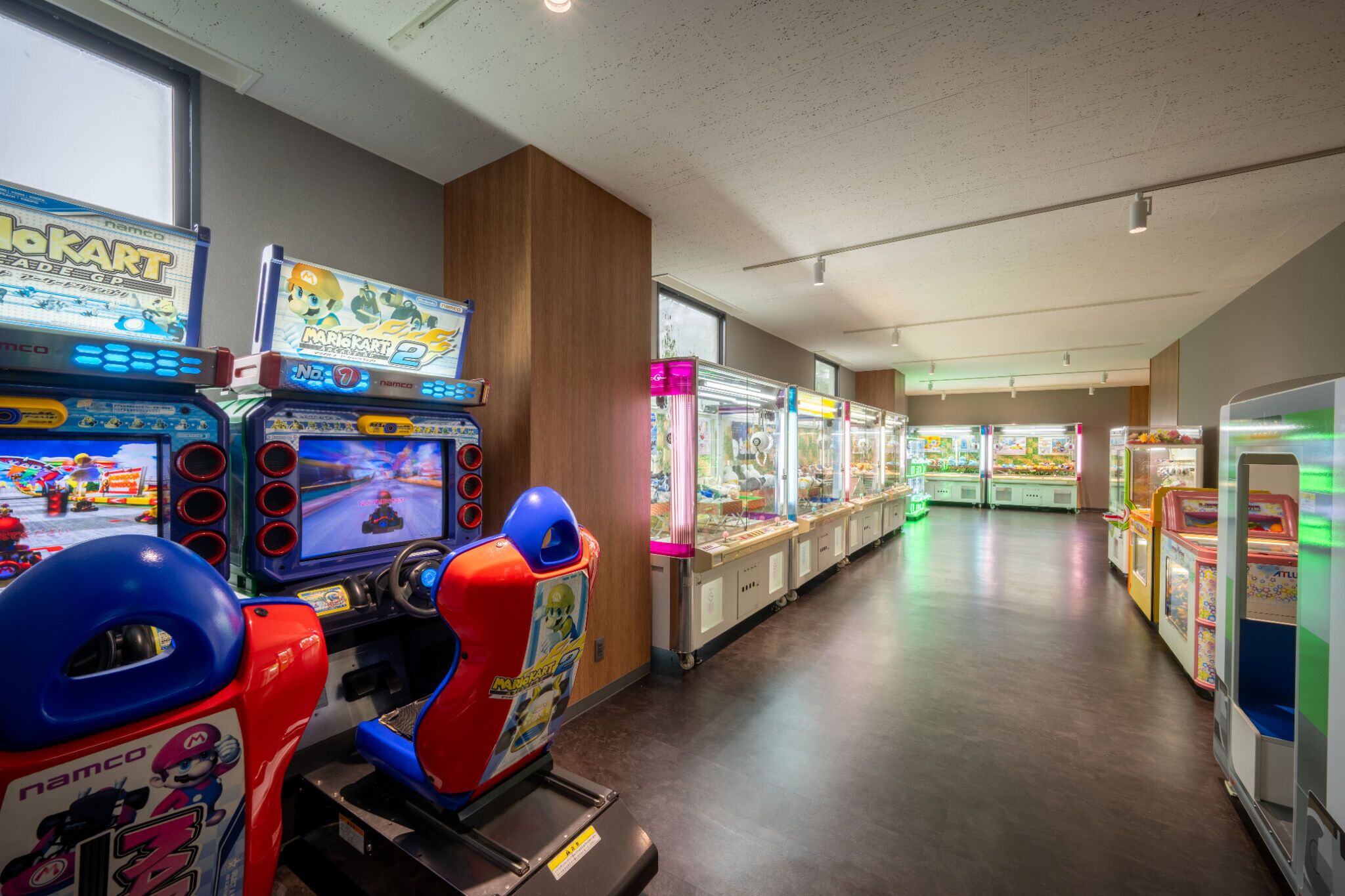 A row of arcade games in a brightly lit indoor space with wooden paneling and large windows.