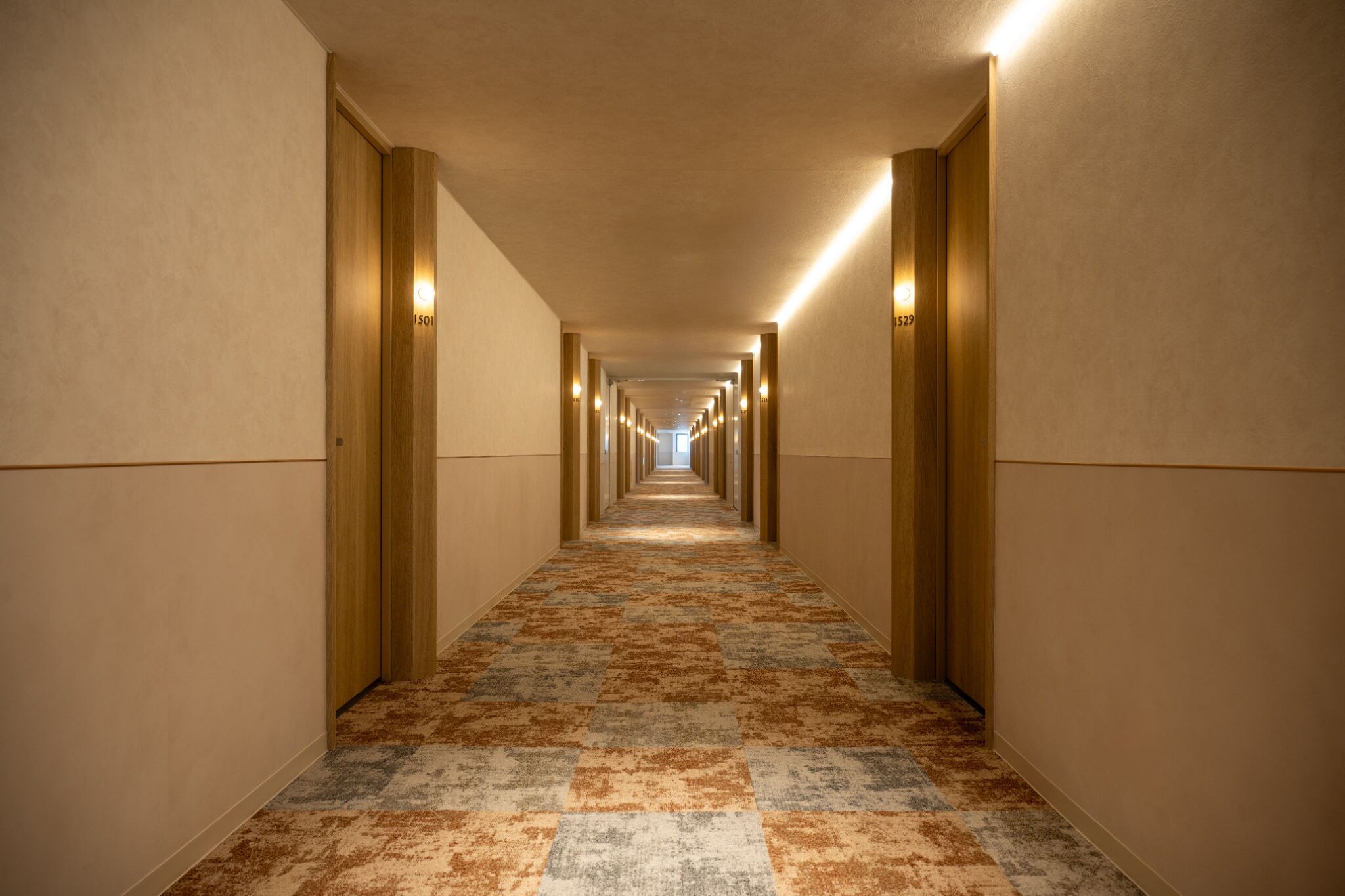 A long, narrow hotel corridor with carpeted flooring and wooden walls.