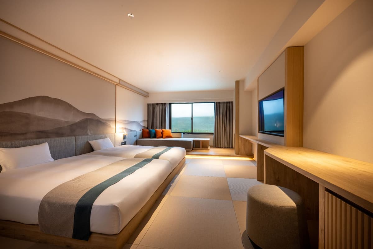 A hotel room with a large bed, a TV, a seating area with a view, and a wooden desk.