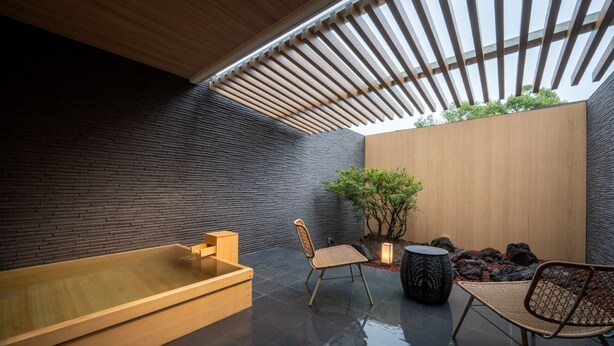 Een moderne spa-ruimte met een houten bad, twee rieten stoelen, een bijzettafeltje en een potplant.