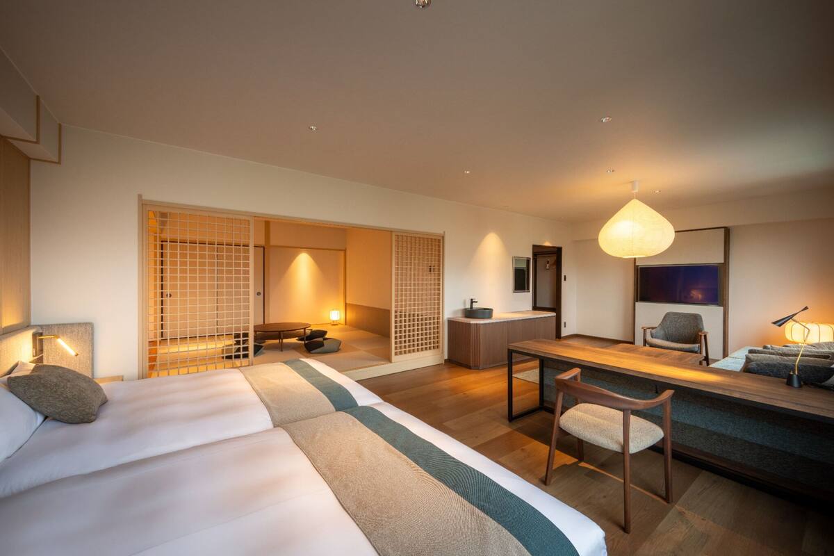 A hotel room with a bed, a desk, a chair, a sofa, a small table, and a hanging light fixture.