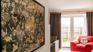 A room with a large framed artwork on the wall, a red sofa, and a view through a glass door to an outdoor area.