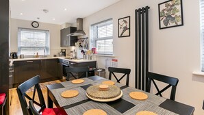 A compact kitchen with modern appliances, a dining area with a table set for four, and a large window providing natural light.