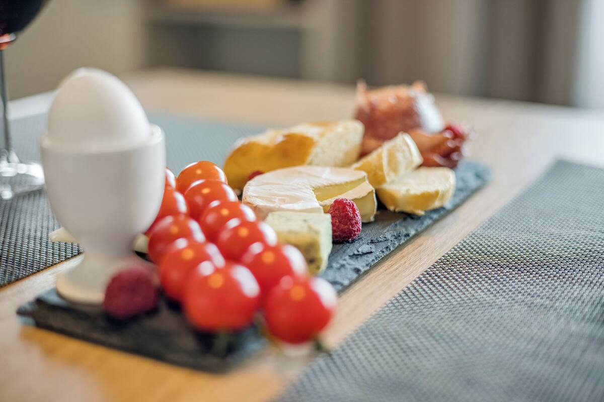 A cheese board with various cheeses, grapes, and a glass of wine on a table.