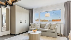 A modern living room with a sofa, a round coffee table with fruit, a large window with a view, and a tall floor lamp.
