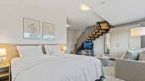 A modern bedroom with a large bed, a TV, and a staircase leading to an upper level.