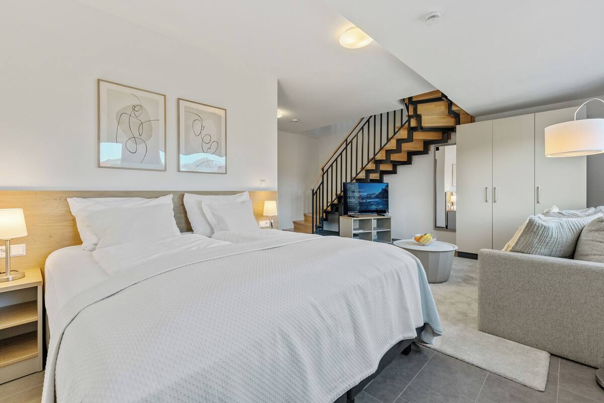 A modern bedroom with a large bed, a TV, and a staircase leading to an upper level.