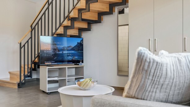 A modern living room with a TV, a sofa, a coffee table, and a staircase.