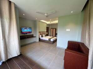 A hotel room with a bed, a TV mounted on the wall, a ceiling fan, and a seating area with a brown leather couch.