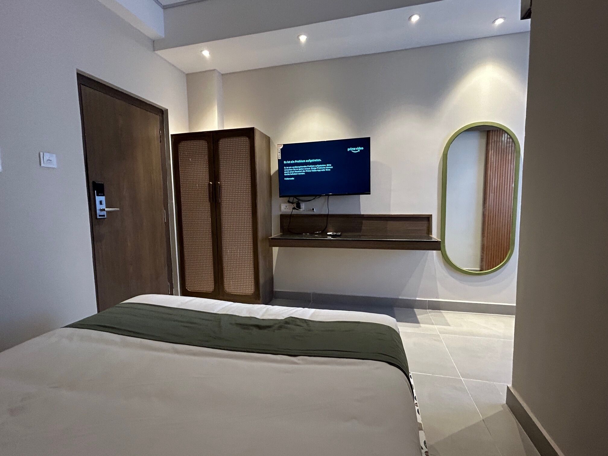 A bedroom with a bed, a television on a stand, a wardrobe, and a mirror on the wall.