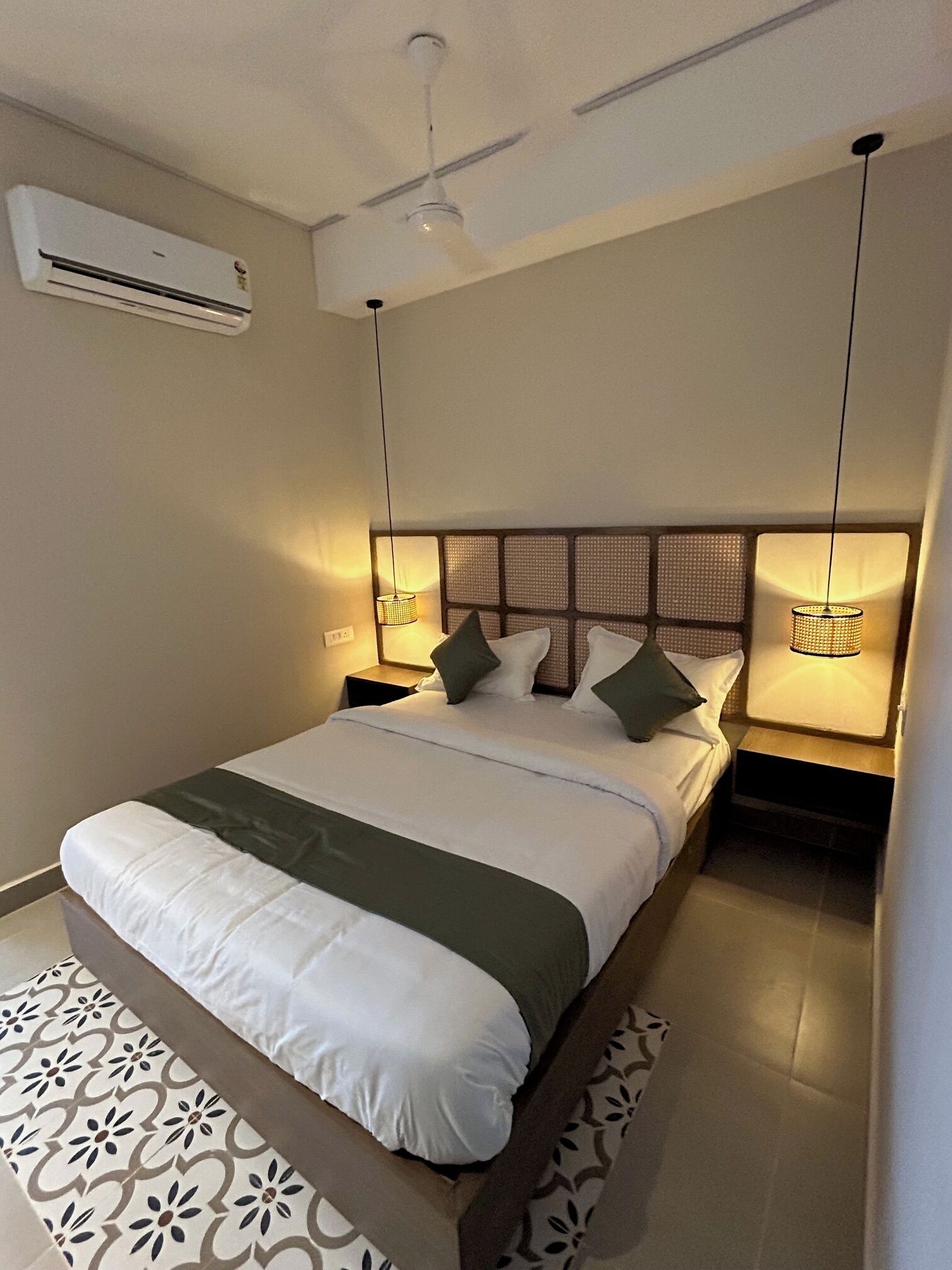 A modern hotel room with a large bed, a ceiling fan, an air conditioning unit, and bedside lamps.